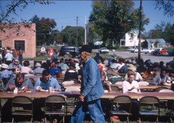 Actors and crew eating lunch in downtown Fort Scott, Kansas. Actor in denim jacket and overalls walks in front.
