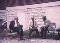 Actor Russell Thorson (Judge Cavanaugh) on left, and two other actors (likely playing jurors) sitting next to the courthouse in the trial scene.