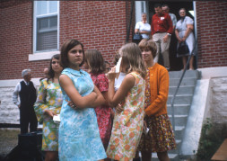 Young women stand in front of the courthouse from the trial scene. The individuals are likely visitors to the set, as they are not present in the trial scene, nor dressed in clothing appropriate for the film‚Äôs time setting.