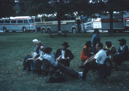 Acting cast, including Estelle Evans (Sarah Winger) on the far right, Stephen Perry (Jappy) standing in blue shirt and overalls, and Malcolm Atterbury (Silas Newhall) in black suit and hat, seated in front of production vehicles.