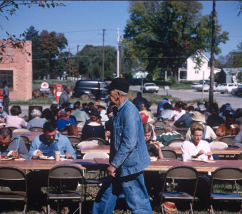 Actors and crew eating lunch in downtown Fort Scott, Kansas. Actor in denim jacket and overalls walks in front.