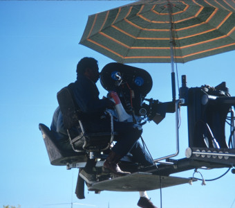 Director Gordon Parks filming a scene from above under striped umbrella.