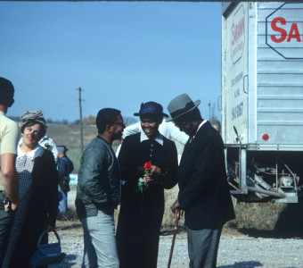 Actresses S. Pearl Sharpe (Prissy) wearing a long black dress, talks with actor Joel Flullen (Uncle Rob) and others. This photograph was likely taken around the filming of Sarah Winger‚Äôs funeral scene.