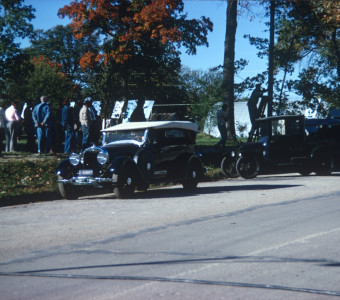 Antique cars parked along the street with actors in the background.