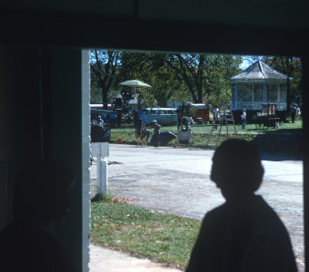 Silouette of a woman in a doorway looking out on the production crew preparing to film in a local park located in Fort Scott, Kansas.