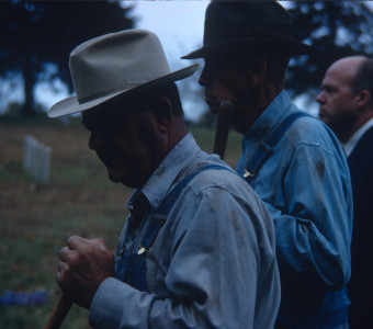 Two Actors in overalls and wearing hats in a shadow.