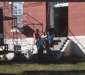 Crew members and production equipment outside of courthouse building from trial scene.