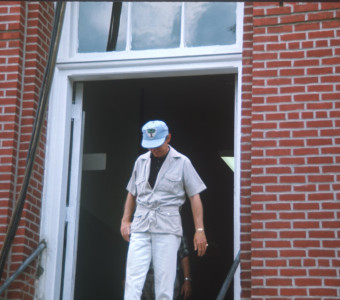 Crew member in Learning Tree hat exiting courthouse building from trial scene.