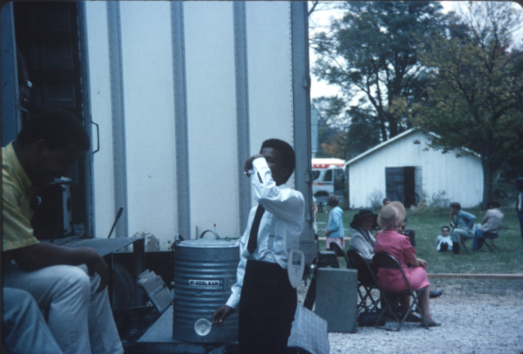 Actor Kyle Johnson (Newt Winger) taking a drink, while other actors sit in the background.