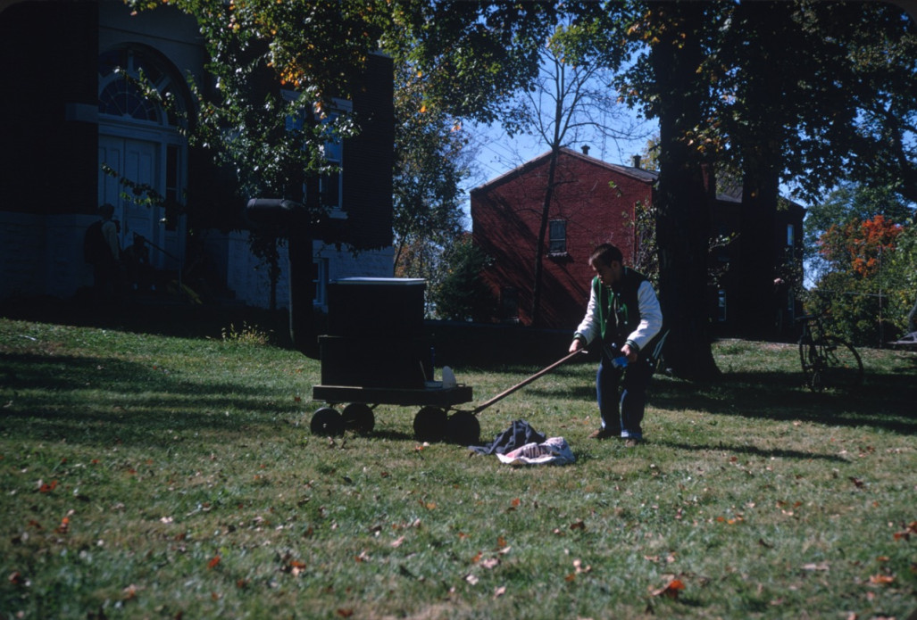 Production crew member outside of the courthouse from the trial scene moves something with a wagon.