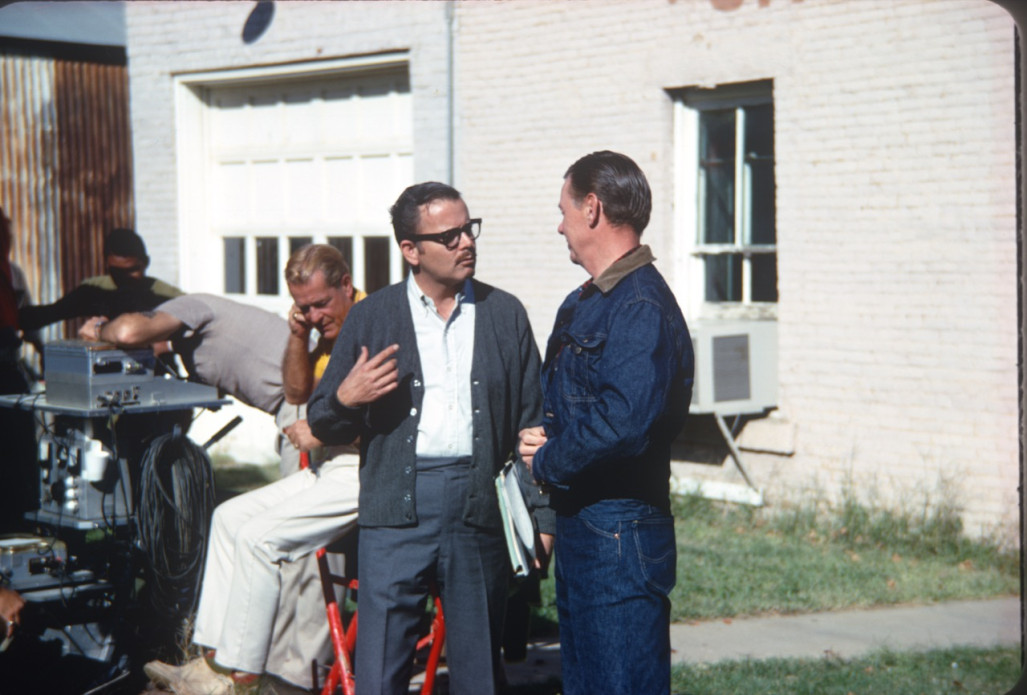 Production crew member conversing with actor George Mitchell (Jake Kiner) dressed in blue denim jacket and jeans, in downtown Ft. Scott, Kansas.