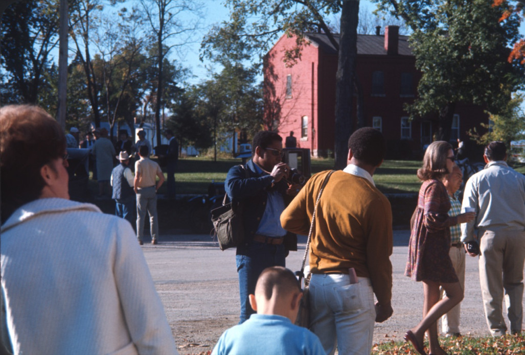 Actor Kyle Johnson (Newt Winger), facing away from the camera, is photographed byGordon Parks' oldest son, Gordon Parks Junior. Various actors and crew members mingle in the street in front of a red brick house.