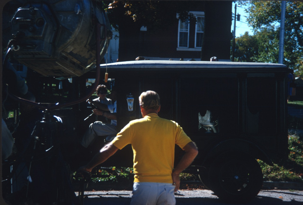 Crewmember in Yellow T-shirt with filming equipment by antique hearse.