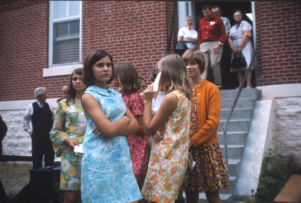 Young women stand in front of the courthouse from the trial scene. The individuals are likely visitors to the set, as they are not present in the trial scene, nor dressed in clothing appropriate for the film‚Äôs time setting.