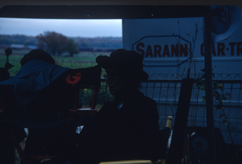 Actress, obscured, seated amongst production equipment.