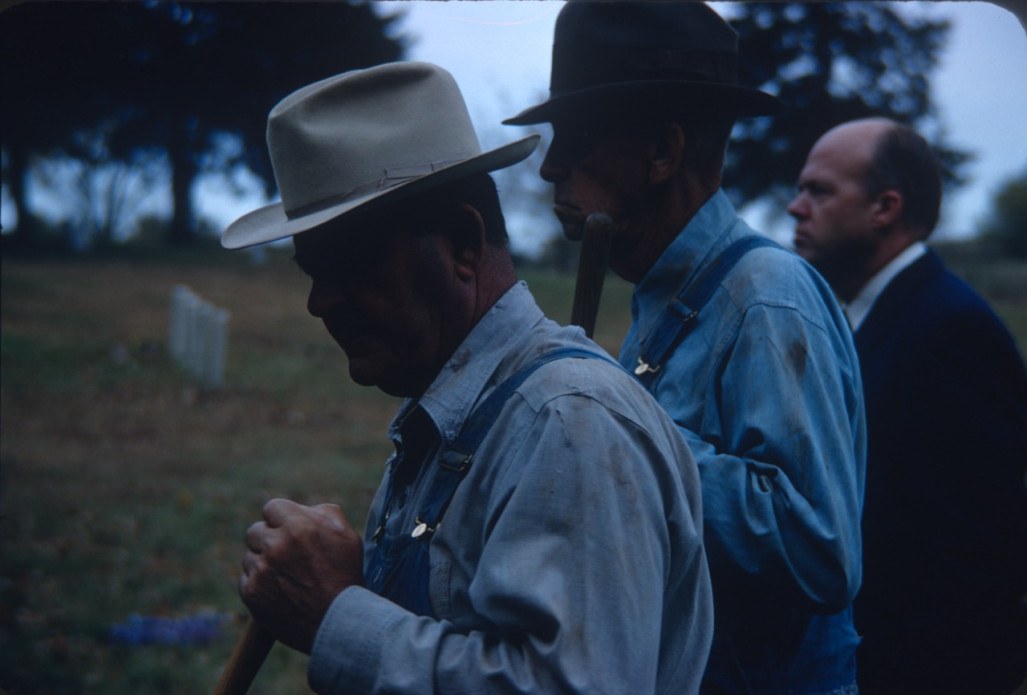 Two Actors in overalls and wearing hats in a shadow.