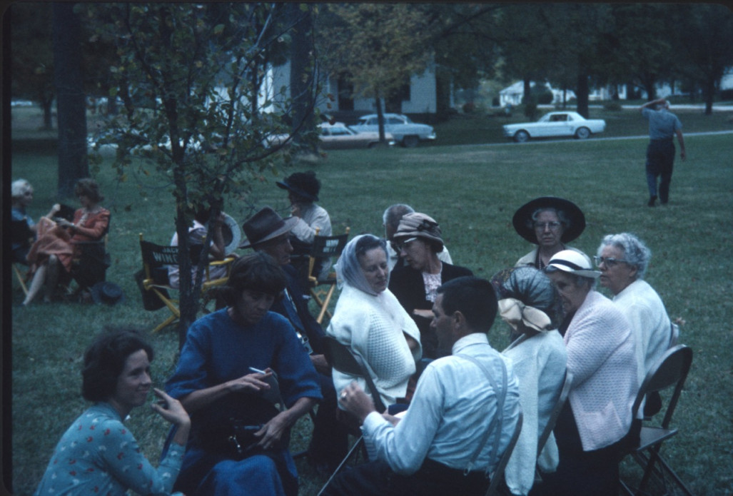 Acting cast members seated in chairs on lawn.