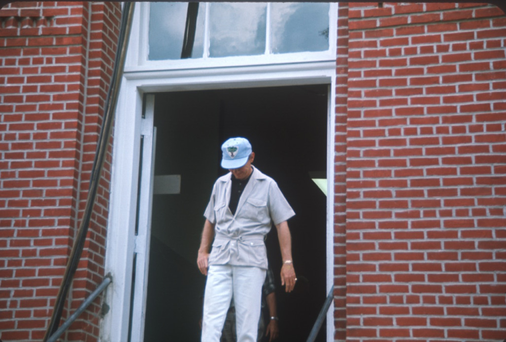 Crew member in Learning Tree hat exiting courthouse building from trial scene.