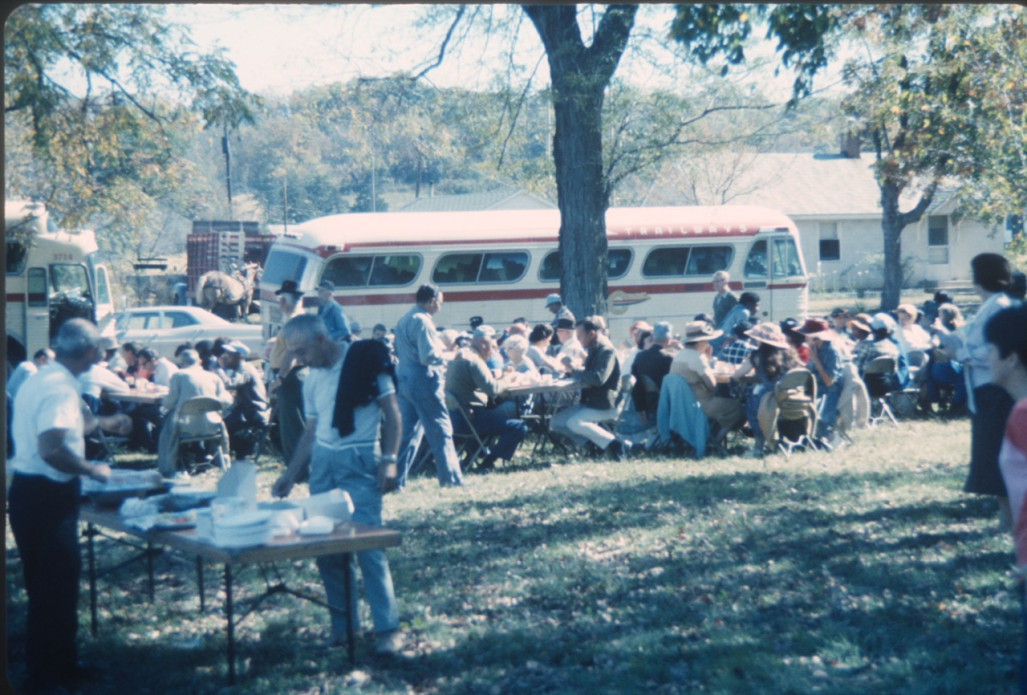 Cast and crew eating a meal outside by production buses.